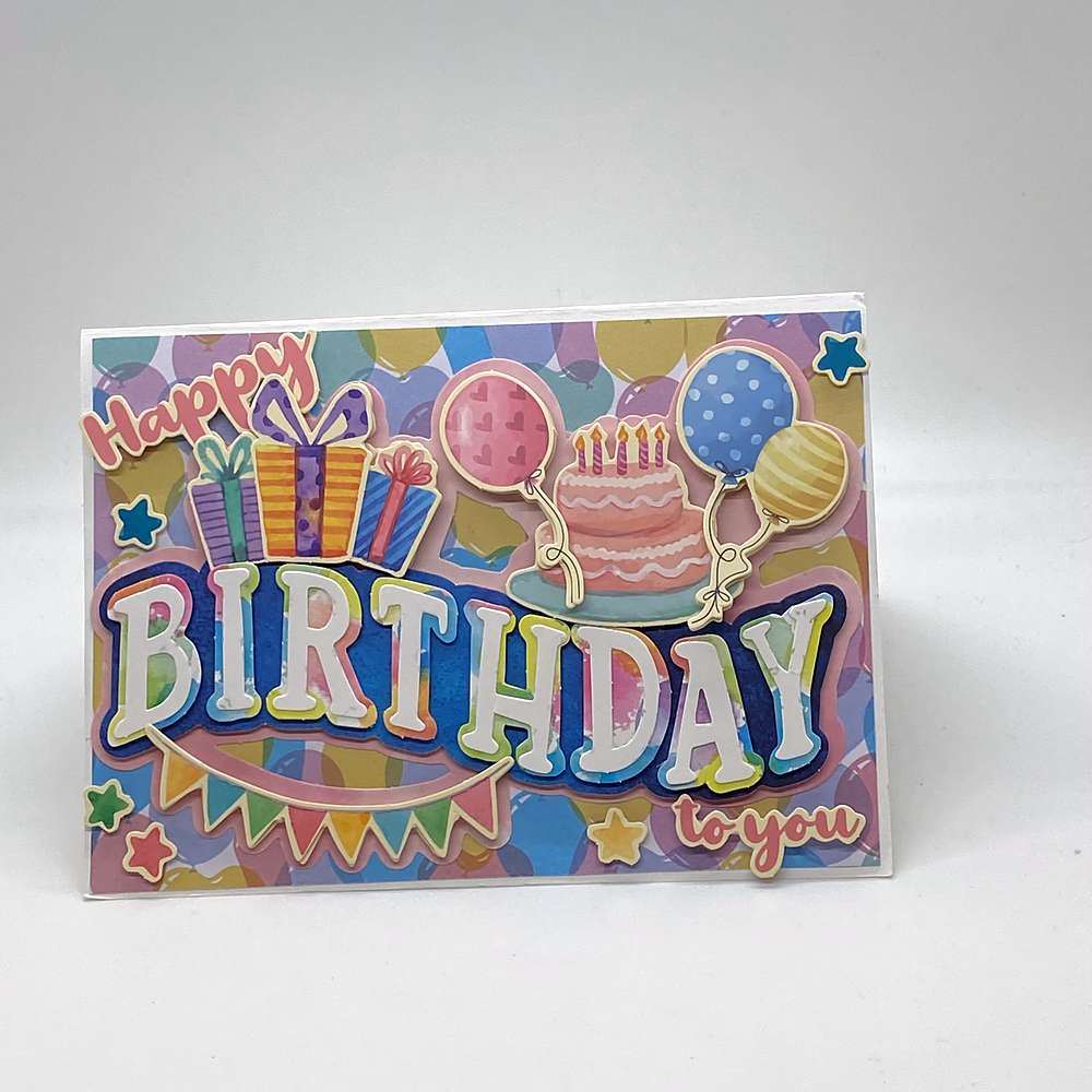 3D birthday card in landscape format with colorful balloon patterned paper, raised puffy letters, stacked gift boxes, a pink layered cake, three balloons, a pennant banner and stars. Text reads: "Happy Birthday to you" - Grammy's Grams Handmade Greeting Cards